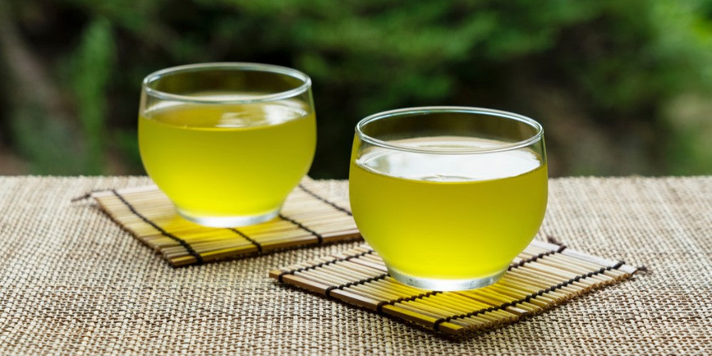 2 Gläser mit kalt gebrühtem Grüntee auf Bambusuntersetzern.