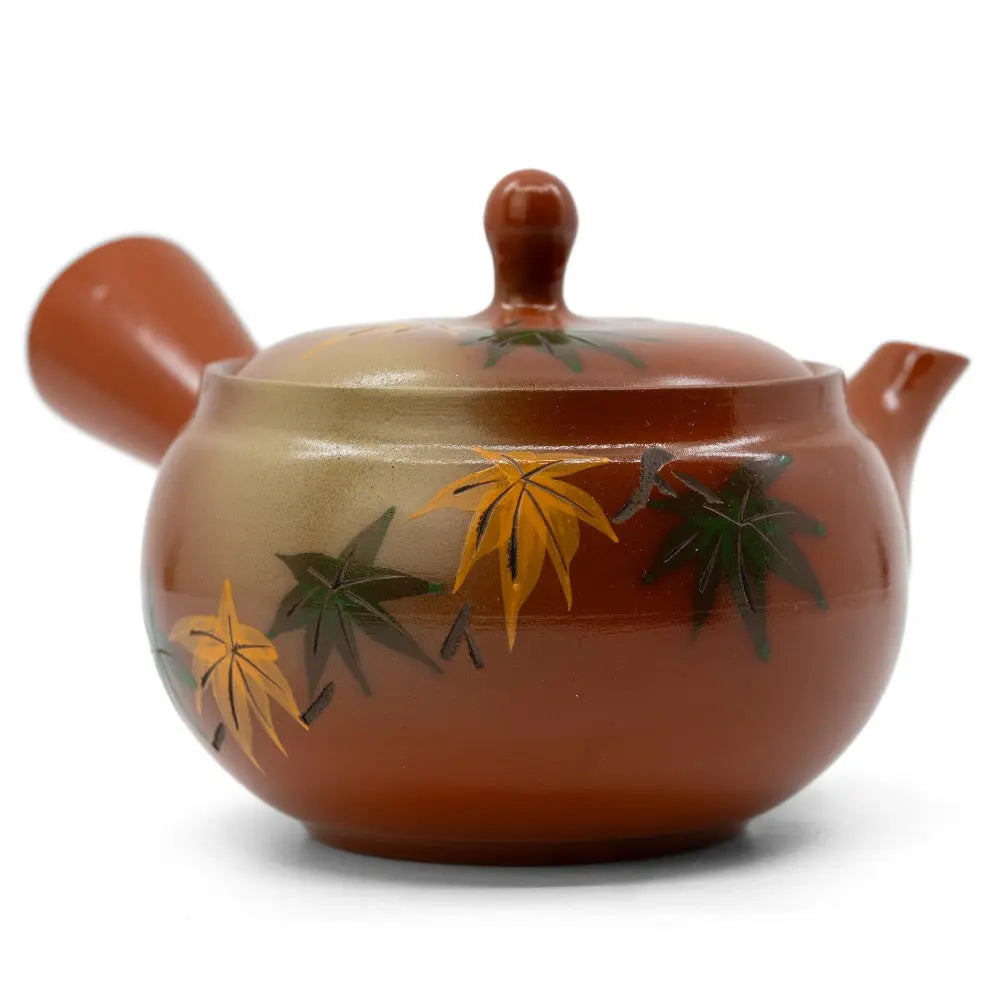 Eine rote Kyusu Teekanne mit gelbem und grünem Herbstlaub darauf abgebildet.